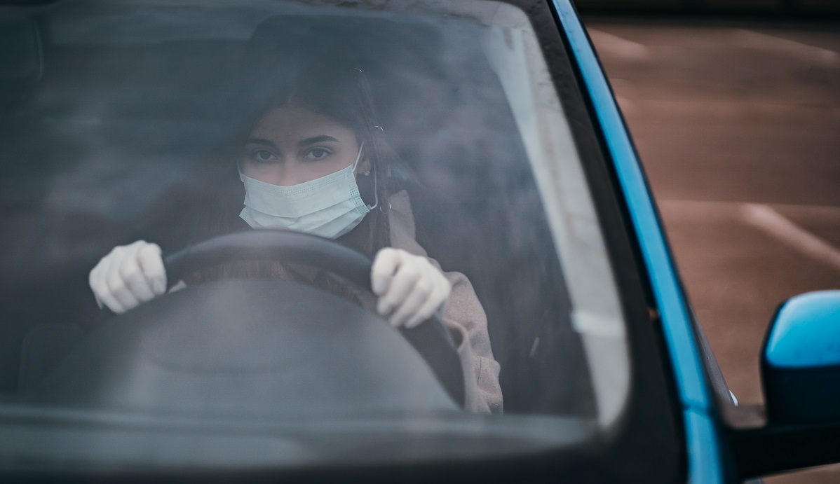 Young woman in a mask and gloves driving a car.